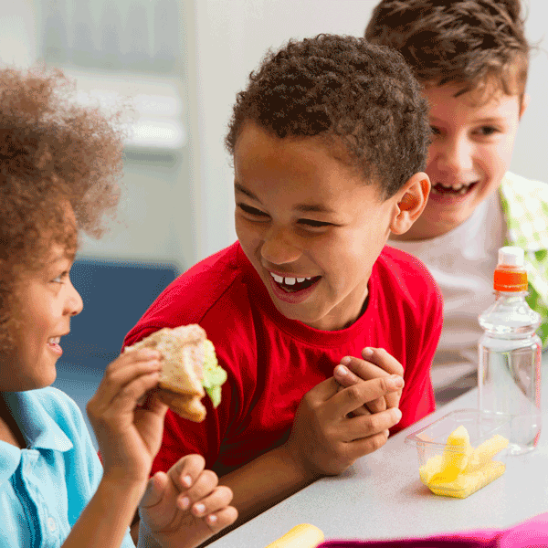 cropped-Schulessen1.png Schulfrühstück: mehrere Kinder essen und lachen